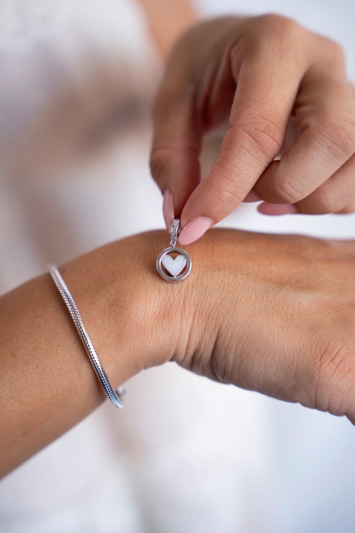 Finger halten den runden silbernen Eline-Charm mit Muttermilchherz über der Hand.