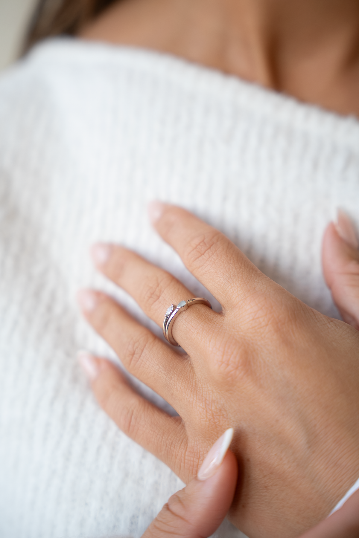 Hand auf weißem Strickpulli, am Finger die silberne Ausführung des offenen Muttermilchrings Naomi