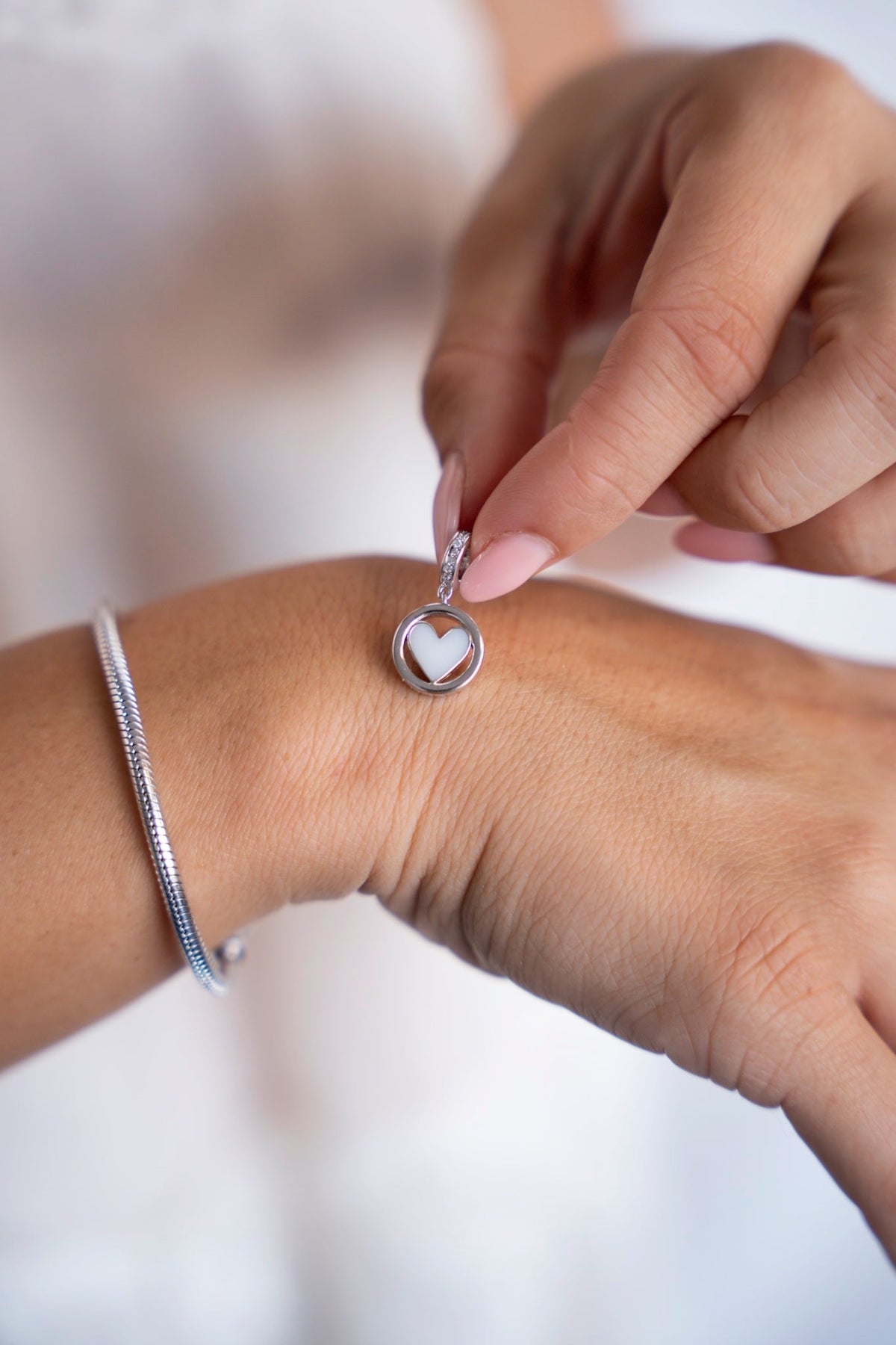 Eline-Muttermilch-Charm aus 925er Silber mit herzförmiger Muttermilch in einem runden Rahmen, neben einem Armband.