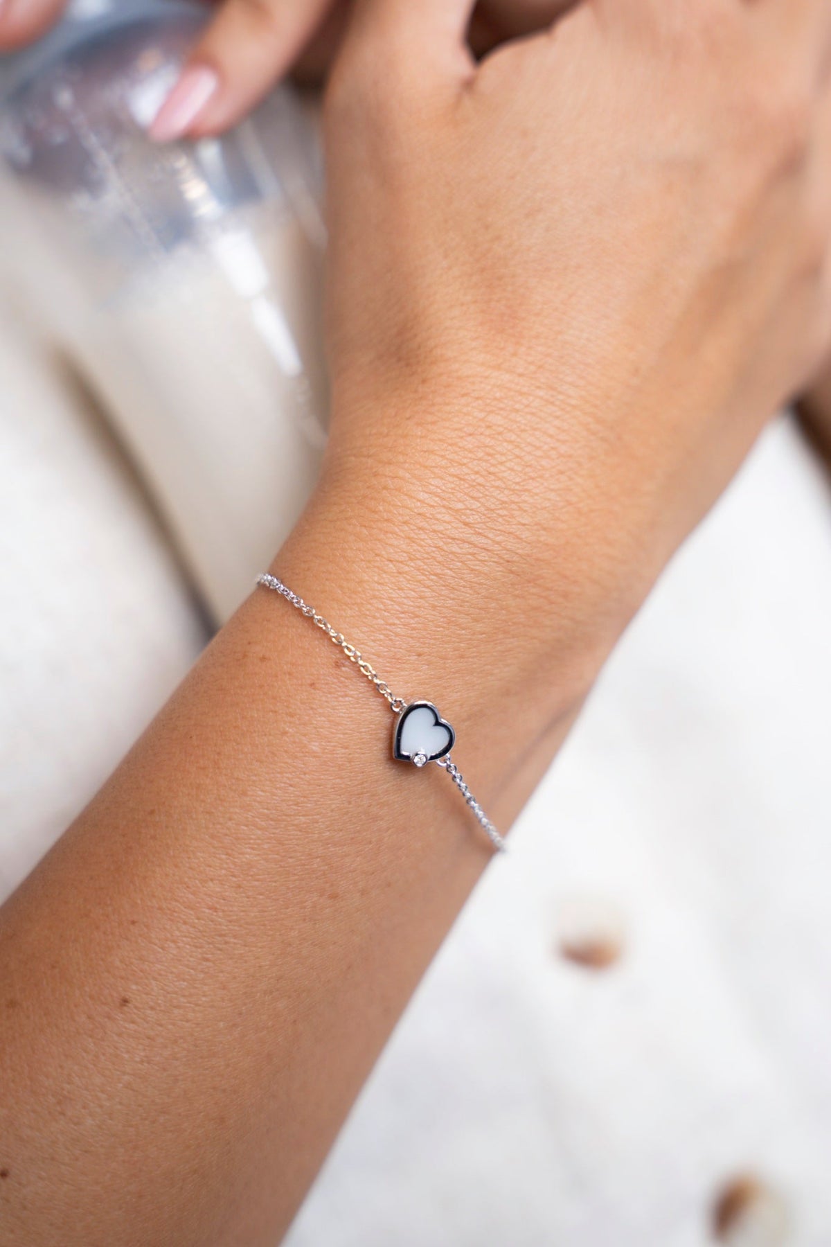 Silbernes Esmée-Armband mit herzförmigem Muttermilchstein am Handgelenk, neben einem Fläschchen Milch.