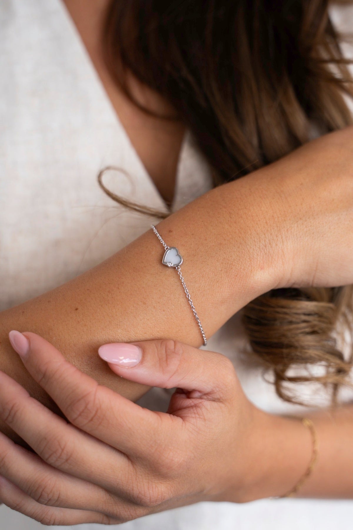 Esmée-Armband aus 925er Silber mit Muttermilchherz, am Handgelenk vor einem Leinentop getragen.