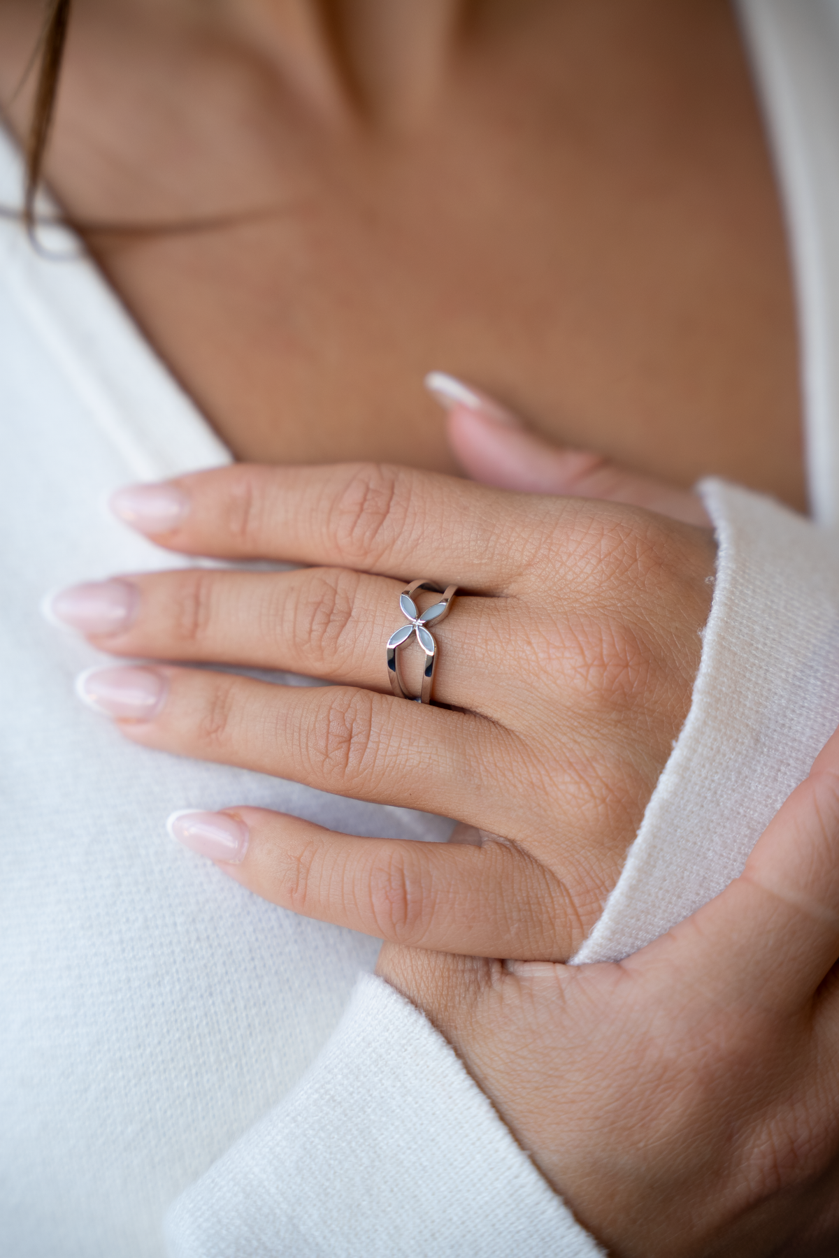 Hand auf der Brust einer Frau im weißen Strick, am Ringfinger der Fleur Muttermilchring mit geteiltem Band