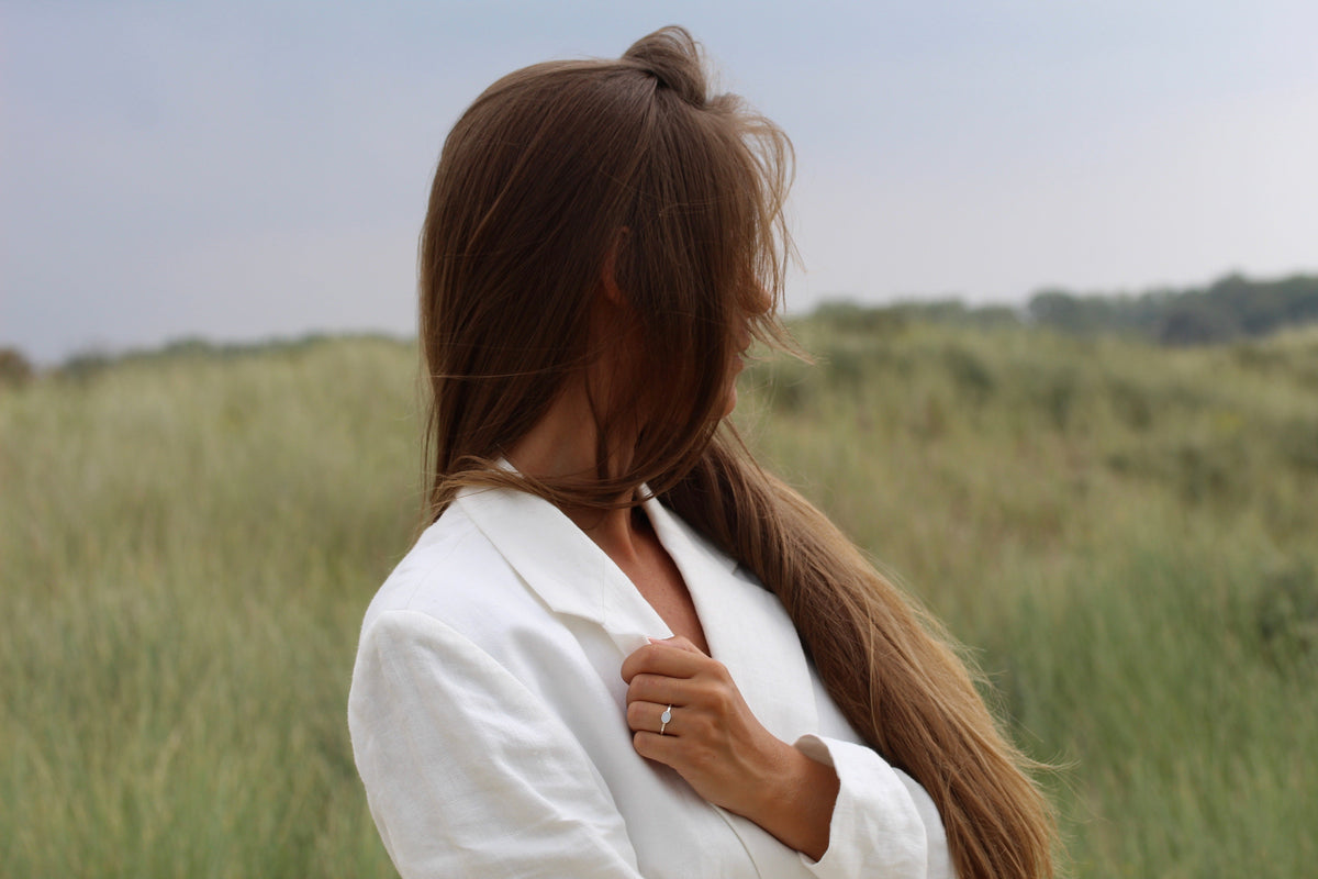 Frau in den Dünen mit Haar vor dem Gesicht, am Ringfinger ein silberner Muttermilchring