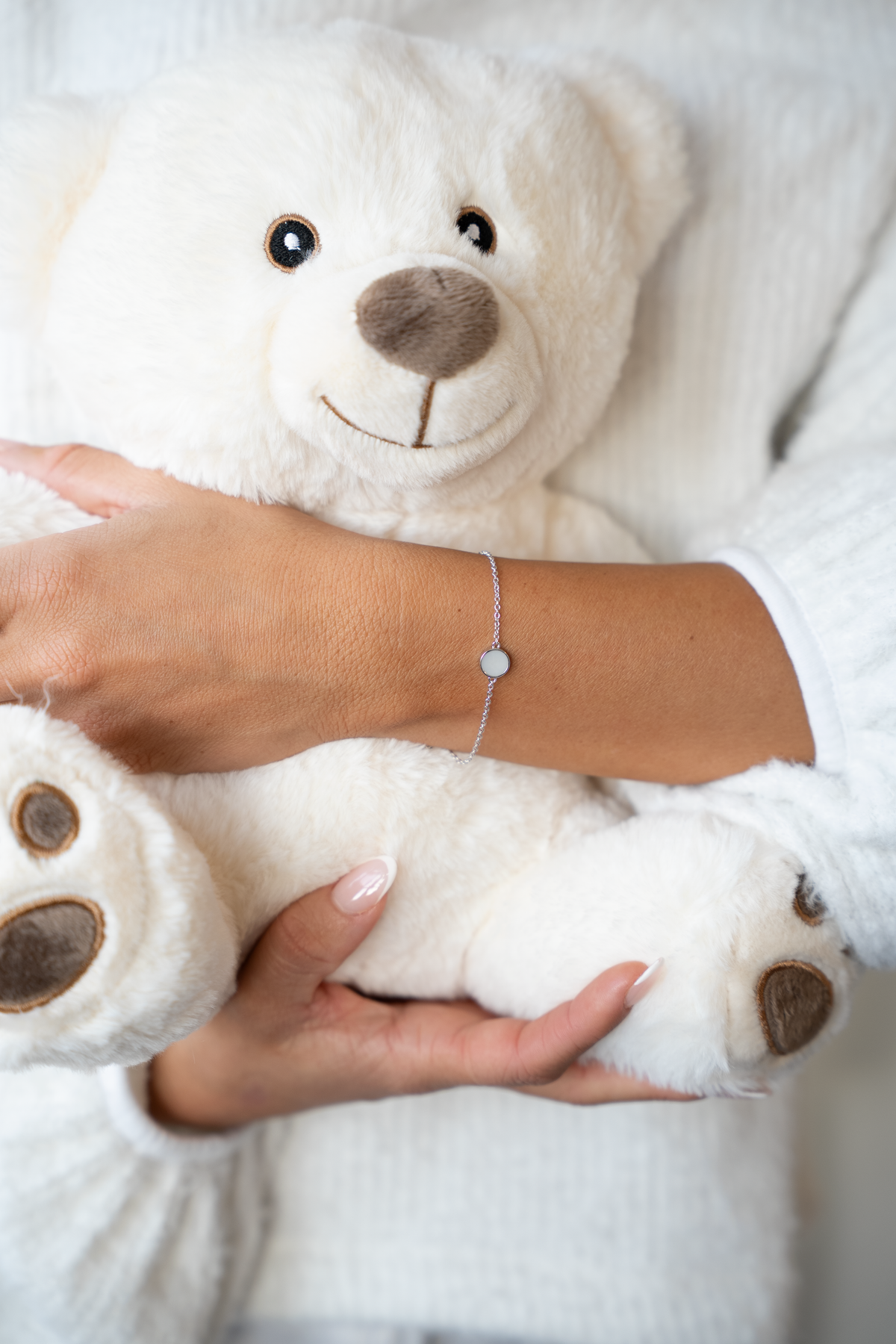 Frau hält einen weißen Teddybären und trägt das silberne Armband Lis mit rundem Muttermilchstein am Handgelenk.