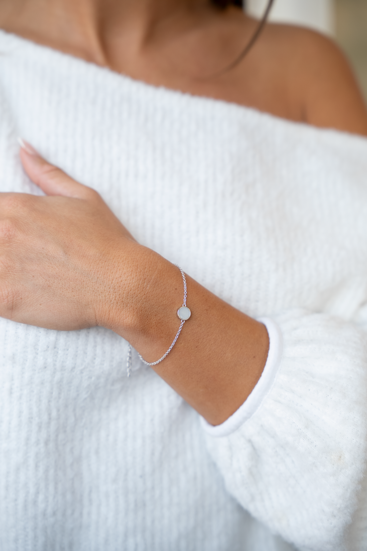 Silbernes Armband mit runder Muttermilch-Kunstharzfläche, zart und filigran, an einem Handgelenk getragen.