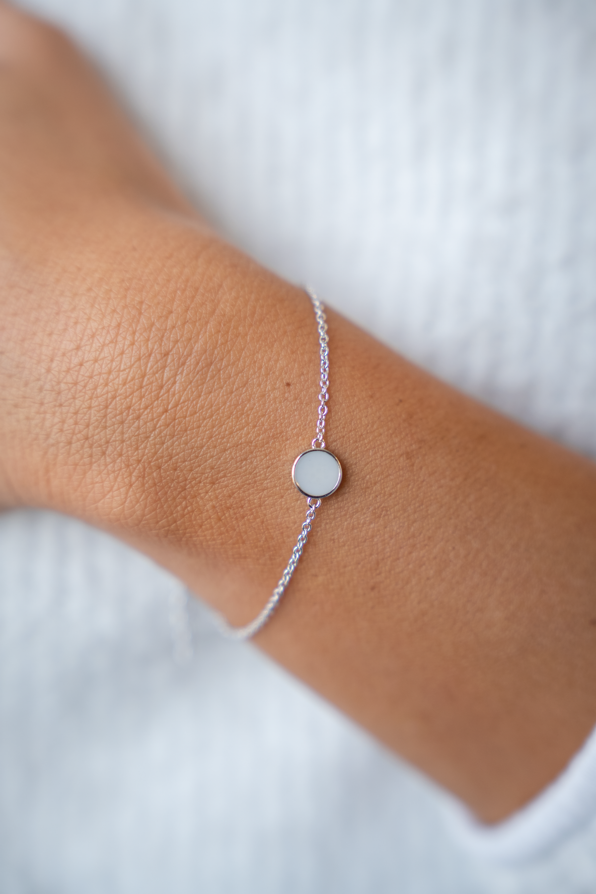 Nahaufnahme des Armbands Lis am Handgelenk: flacher runder Muttermilchstein in schmalem Rand an feiner Kette.