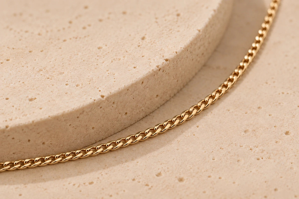 Kette aus gelblich-goldenem Metall mit geflochtenem Design, auf einer hellen, strukturierten Oberfläche drapiert.