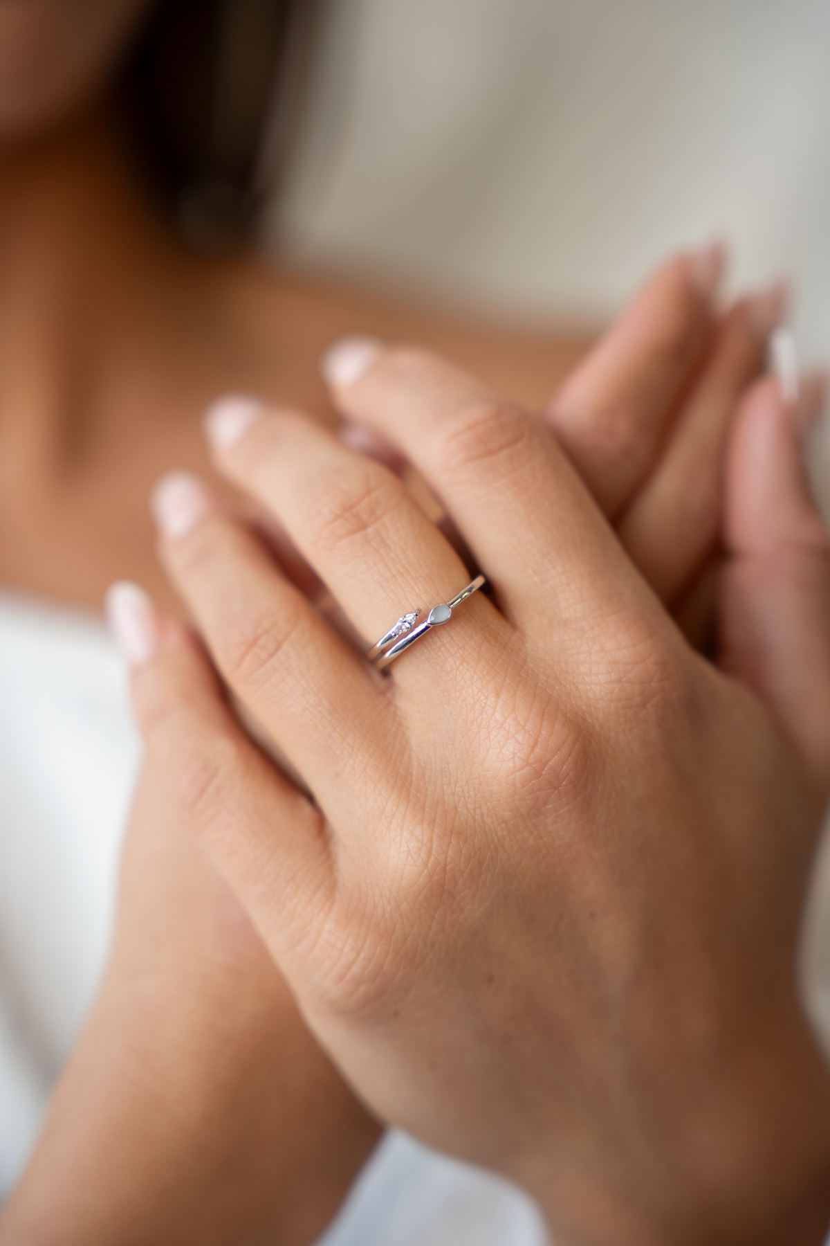 Gefaltete Hände, am Finger der offene Ring Naomi mit Muttermilchtropfen und klarem Marquise-Stein